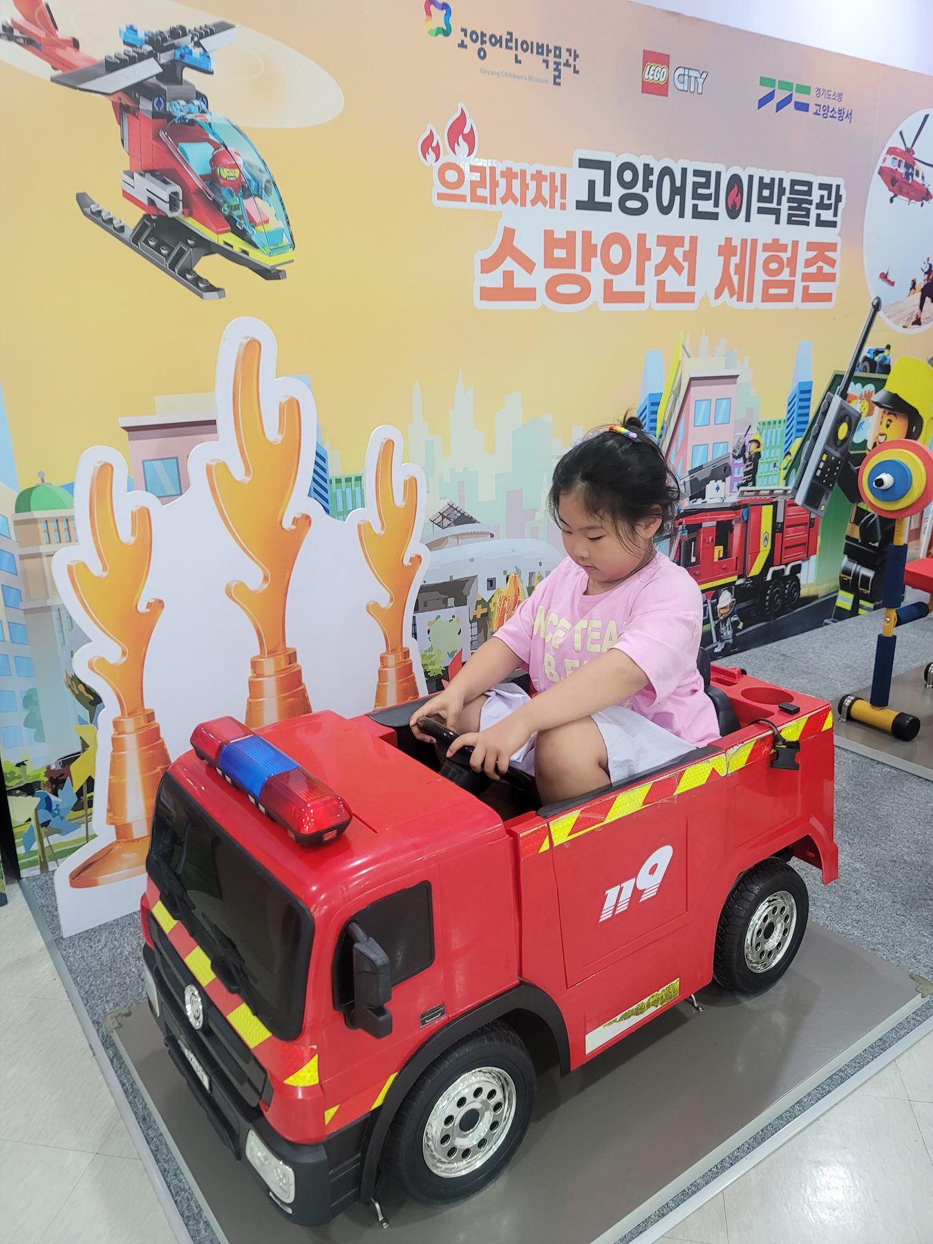 A child driving a toy fire engine in the fire safety experience zone at Goyang Children's Museum