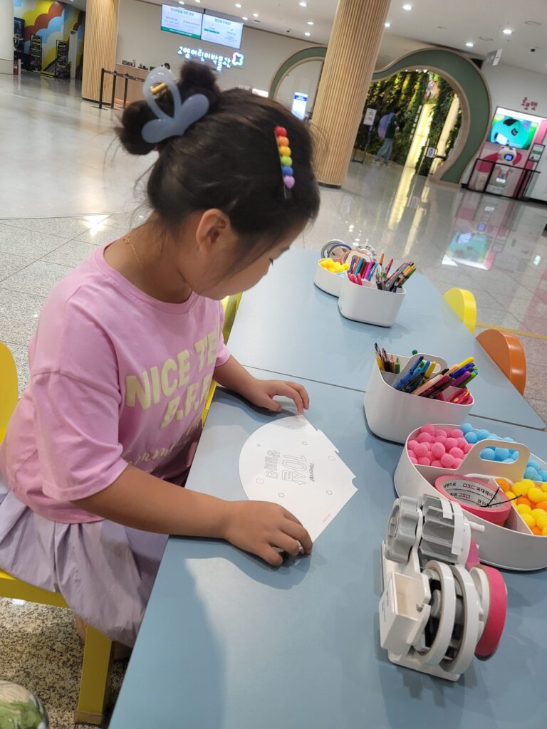 Child making a paper craft at a table in the lobby of Goyang Children's Museum