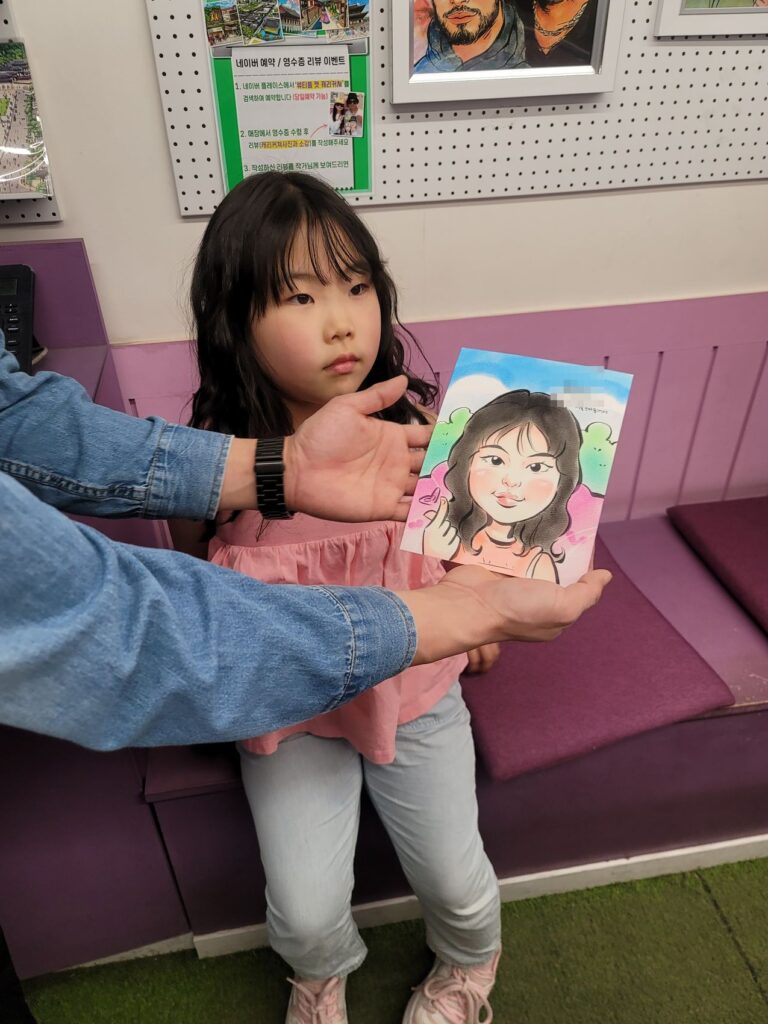 A child holding the finished watercolour caricature portrait drawn in Insadong