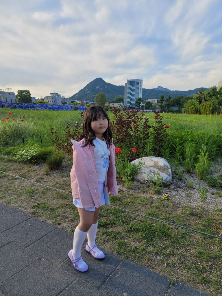 A child standing on a path at Songhyeon Green Plaza with mountains rising behind the city